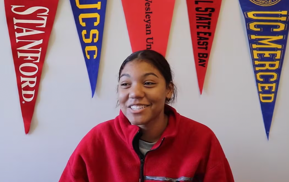 Student smiling at the camera, with a variety of college banners in the background